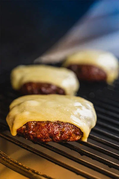 Juicy burger patties with melted cheese grilling on barbecue grate, seasoned with all-natural BBQ rubs