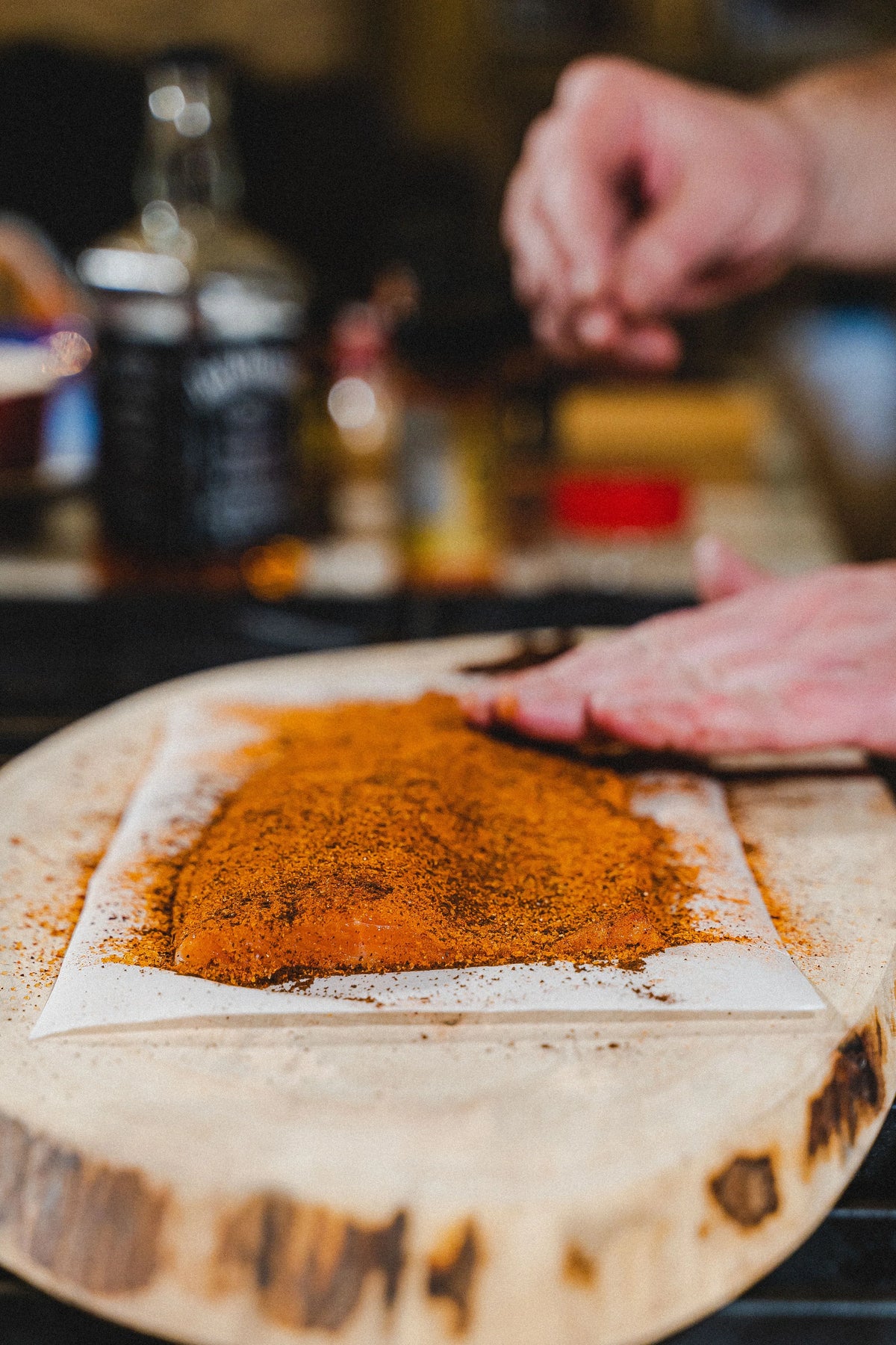 Hands seasoning raw meat with all-natural BBQ rub on parchment paper, perfect for grilling.